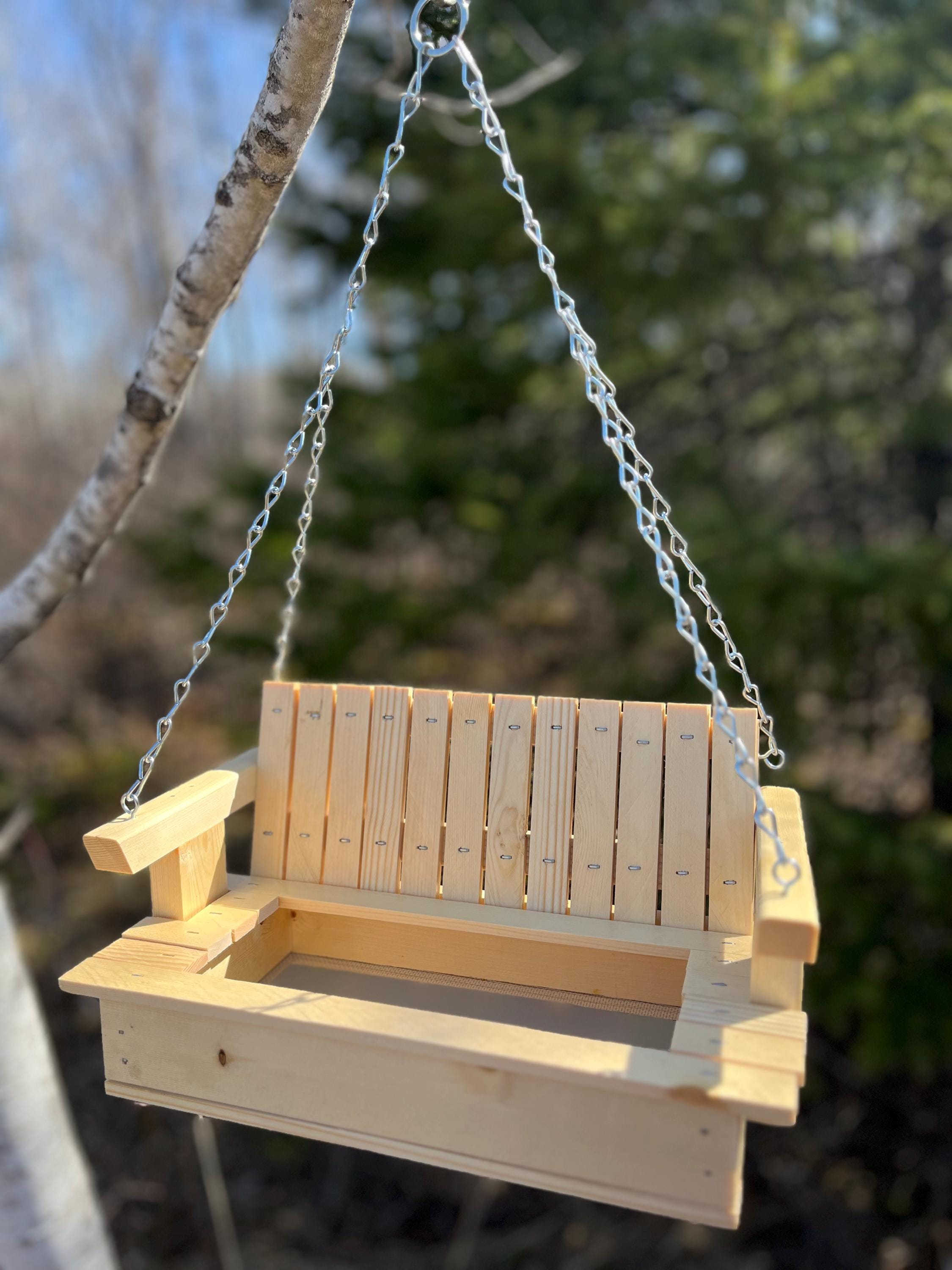 Natural clear-coat pine porch-swing bird feeder hanging from a birch branch in the woods.